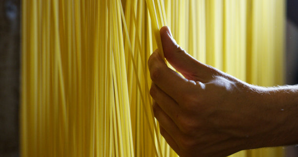 早上，一个小男孩用手触摸新鲜的意大利面，把它们晾干，以确保高质量图片下载