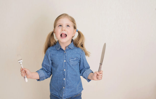 小女孩拿着刀叉。饥饿的孩子。图片下载