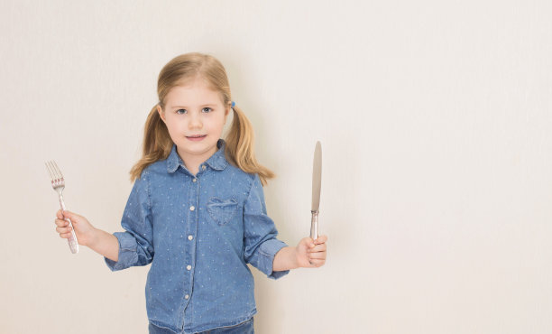 小女孩拿着刀叉。饥饿的孩子。图片下载