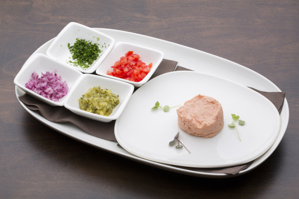 木桌上的白色陶瓷盘子里装着金枪鱼酱、西红柿、黄瓜、洋葱和欧芹图片下载