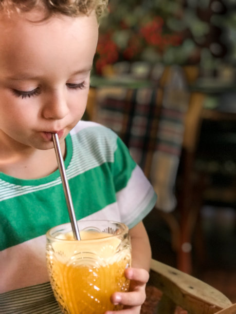 蹒跚学步的孩子用可持续的金属吸管喝橙汁图片下载