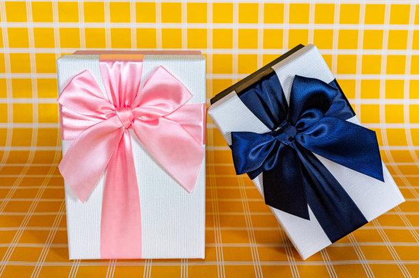 两个白色礼品盒，一个是粉色的，一个是蓝色的，上面有一张黄色格子的背景照片图片下载