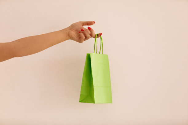 粉红色背景下，女人手中的绿色纸袋图片下载