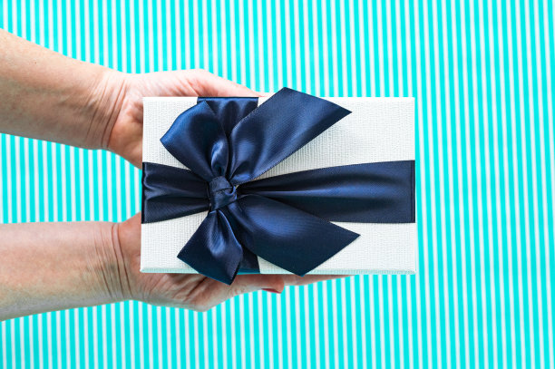 特写女性的手拿着一个白色礼盒与蓝色丝带在绿松石背景的股票照片图片下载