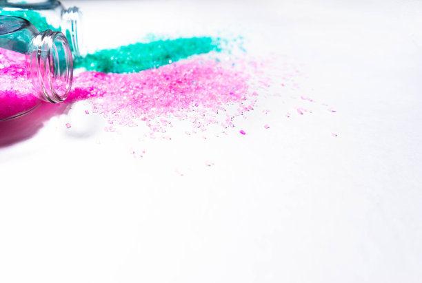 两个装有淡粉色和绿松石浴盐的透明罐子。在画面中，只有物体的上部。白色背景上的水平照片。个人护理和水疗配件的概念。银行倒在一边。的空间图片下载