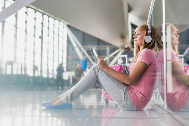 一个十几岁的女孩坐在地板上，戴着耳机看她的数字平板电脑上的电影图片下载