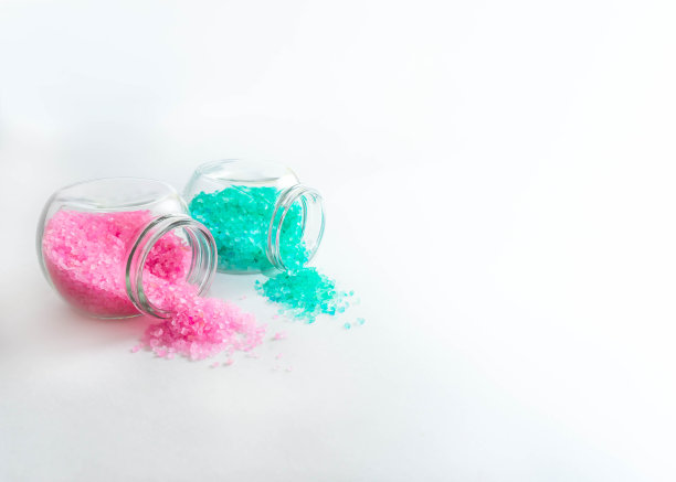 两个装有淡粉色和绿松石色浴盐的透明罐子。白色背景上的水平照片。个人护理和水疗配件的概念。银行倒在一边。空间的文本图片下载