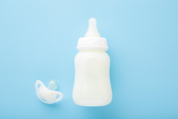 浅蓝色背景上的一瓶白色牛奶和奶嘴。婴儿喂养的概念。柔和的颜色。特写镜头。自顶向下的观点。图片下载