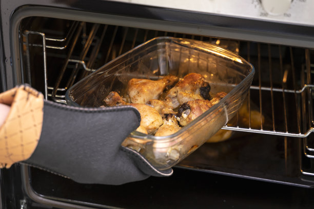 手戴耐火手套从烤箱中拿出一个烤鸡腿盘图片下载