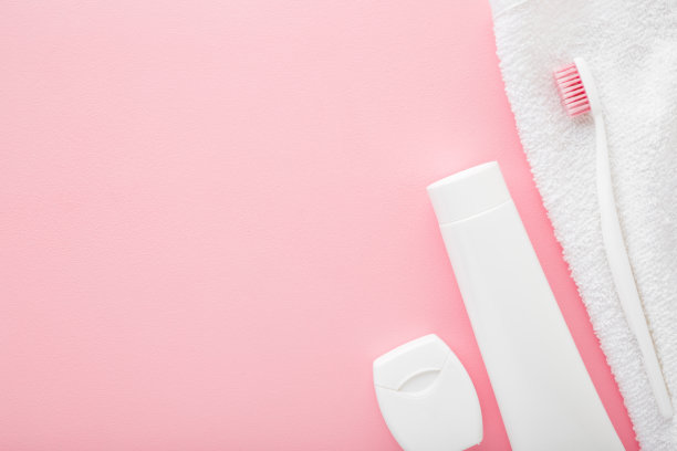 白色的牙膏，牙刷，牙线和毛巾放在浅粉色的桌子背景上。柔和的颜色。人们的牙齿卫生观念。文字或标识的空白位置。特写镜头。前视图。图片下载