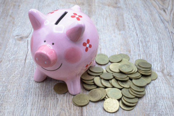 桌子上有许多硬币和粉色的存钱罐，为将来买房子攒钱的想法，积累少量的钱。退休钱图片下载
