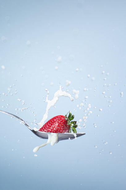 草莓和牛奶一起掉进勺子里，在蓝色的背景上产生飞溅和水滴。图片下载