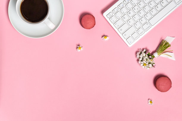 女性的工作空间有键盘，一杯黑咖啡，马卡龙和雏菊花在粉红色的背景，俯视图图片下载