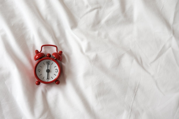 白色皱巴巴的床单上的红色模拟时钟。俯视图，平放，复制空间。水平的。觉醒、睡眠、早起、高效、高效的一天。对于社交媒体，博客。最小的风格图片下载