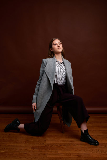 漂亮的年轻女性，穿着经典的套装，黑色的鞋子和灰色的外套。古董椅子。女人的衣服。图片下载