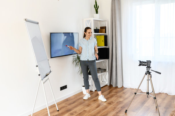 一位妇女正在家里录制教学视频，使用挂图和显示器。三脚架上的相机在女人面前。在线学习的概念图片下载