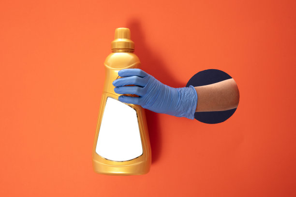 在橙色纸背景的蓝色医用手套拿清洁剂瓶。图片下载