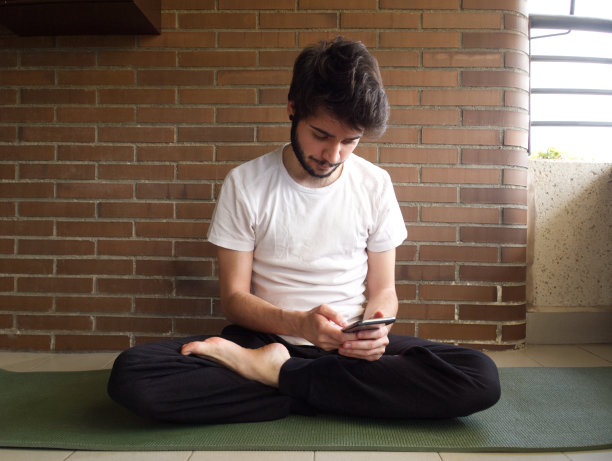年轻英俊的白人男子在看他的智能手机上的瑜伽姿势图片下载