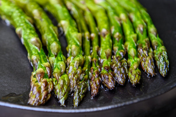 木质背景的黑盘子上放熟的芦笋。选择对焦的照片。图片下载