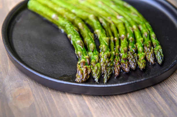 木质背景的黑盘子上放熟的芦笋。选择对焦的照片。图片下载