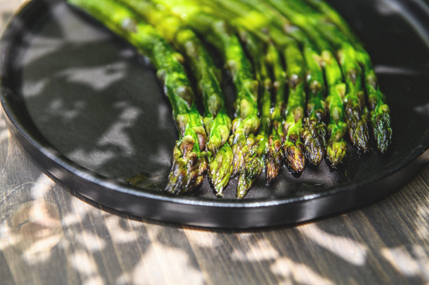 木质背景的黑盘子上放熟的芦笋。选择对焦的照片。图片下载