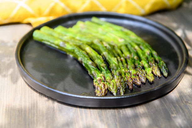 木质背景的黑盘子上放熟的芦笋。选择对焦的照片。图片下载