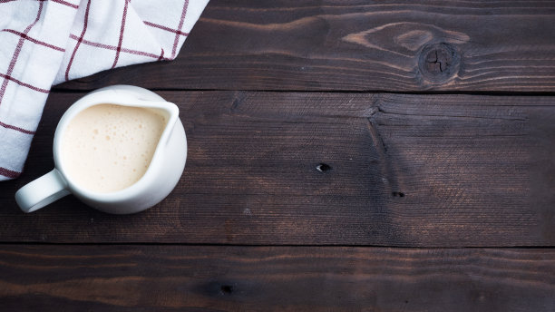 白色陶瓷牛奶壶与新鲜牛奶。深色的木桌。副本的空间。图片下载