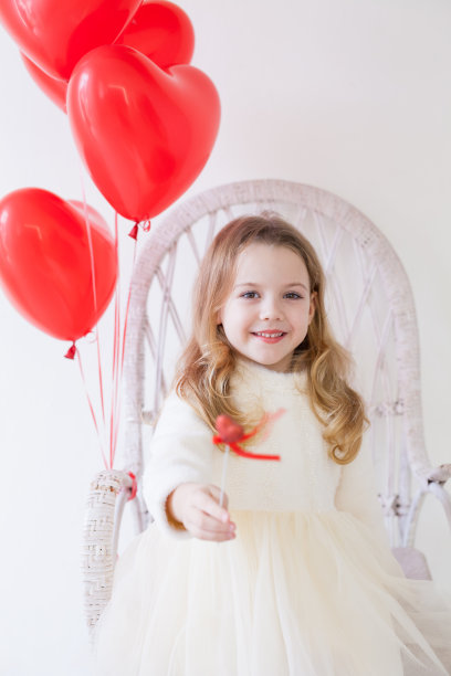 漂亮时尚的小女孩在节日里拿着心形的红色气球图片下载