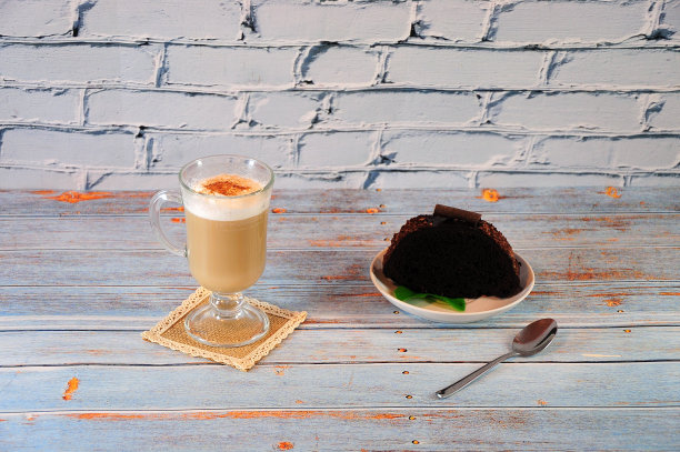 餐巾纸上放着一大杯刚拿铁，木桌上放着一块巧克力蛋糕，盘子里放着一把调羹。图片下载