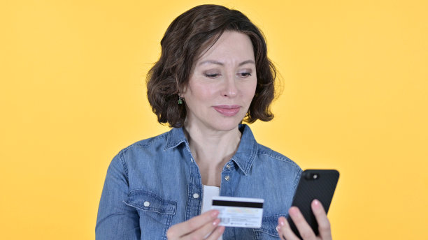 黄色背景的老妇人在智能手机上在线支付图片下载