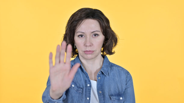 黄色背景上老妇人的停止手势图片下载