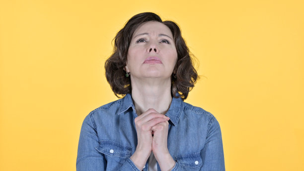 在黄色背景上祈祷的充满希望的老妇人图片下载