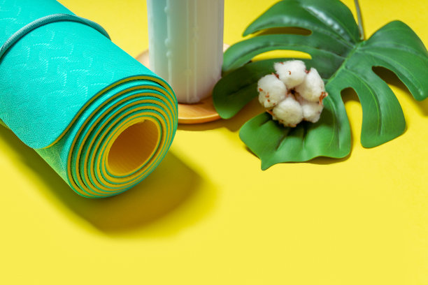 天然木制彩色蜡蜡烛与棉花，绿色的叶子和卷绿松石薄荷瑜伽，普拉提垫在黄色的背景。平铺和文本空间。放松和冥想的概念。图片下载