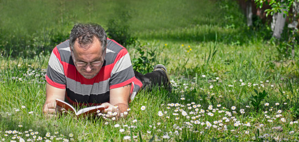 一个男人坐在鲜花盛开的草地上看书。图片下载