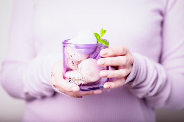 美丽的女性手拿着玻璃杏仁饼干在淡紫色的背景图片下载