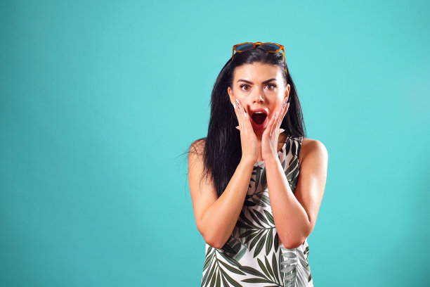 一个快乐的女孩，一头乌黑的直发，表情惊讶，在工作室的蓝色背景下摆姿势图片下载