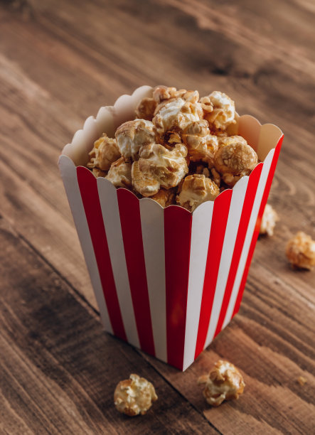 红色和白色条纹盒焦糖爆米花在木制的乡村背景。图片下载