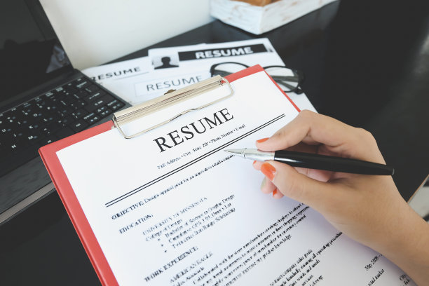 用钢笔特写简历。电脑、笔记本电脑和眼镜放在木头桌子上图片下载