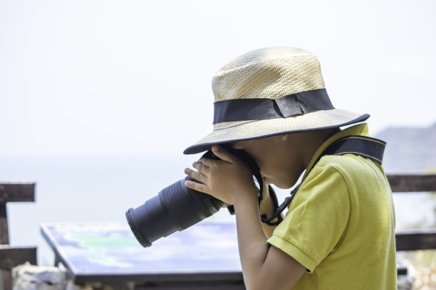 亚洲男孩戴着一顶拿着相机的帽子拍照。图片下载