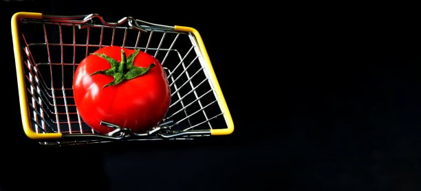一个带有黄色提手的金属篮子，里面有一个黑色背景上的红色番茄，并有放置横幅标签的空间。图片下载