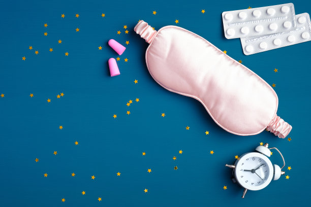 粉红色睡眠眼罩，闹钟，耳塞，失眠安眠药，深蓝色背景和五彩纸屑。睡眠卫生，失眠治疗理念图片下载