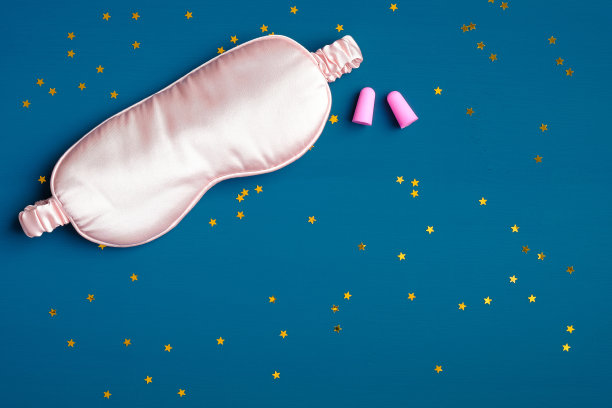 女性睡眠眼罩和深蓝色背景彩纸的粉色耳塞。睡眠用品用于晚安、健康睡眠、失眠治疗图片下载