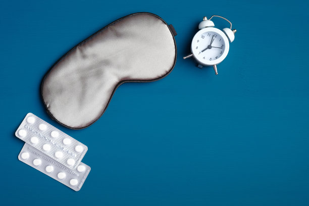 健康睡眠与失眠治疗理念。睡眠眼罩，闹钟，深蓝色背景的安眠药。平躺，俯视图图片下载