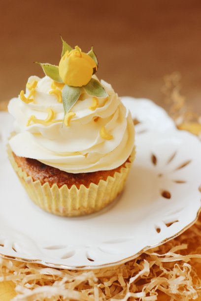 这是一张特写照片，一个黄色的香蕉纸杯蛋糕被放在一个装饰着黄色玫瑰花的白色盘子里。图片下载