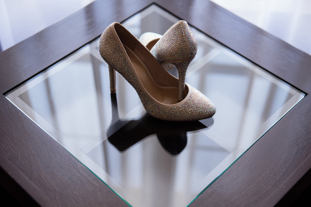 在一张有镜面涂层的深色桌子上放着一双女鞋，鞋上装饰着水钻，为新娘准备的鞋子，窗户反射在镜面涂层上，图片下载