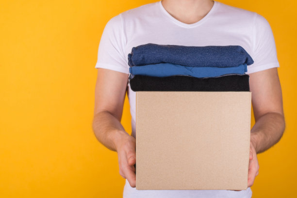 捐赠的概念。裁剪近距离的照片，男子抱着装满衣服的盒子捐赠孤立在黄色背景图片下载