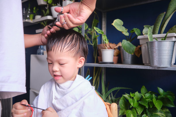 亚洲小男孩在家理发，父亲用剪刀为儿子理发。新冠肺炎健康危机期间隔离期间在家理发图片下载