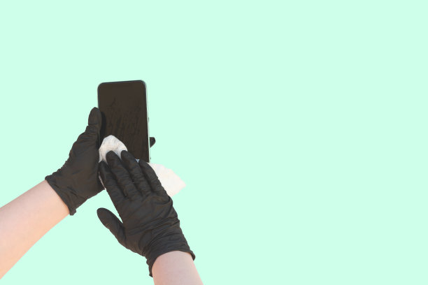 手戴防护乳胶手套，用抗菌湿巾擦拭智能手机图片下载