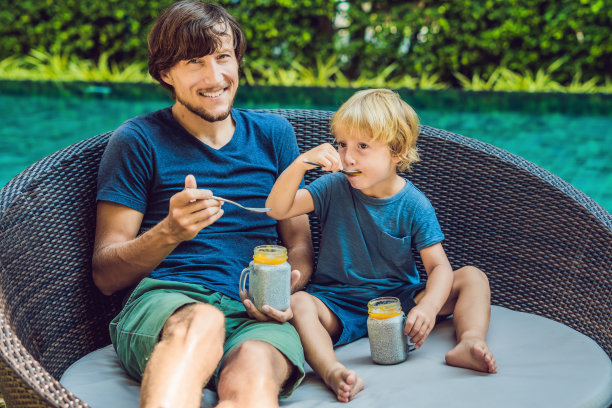 早上，父子俩在池塘边吃着有奇亚籽和芒果的甜点。健康饮食，素食，饮食与人的观念图片下载