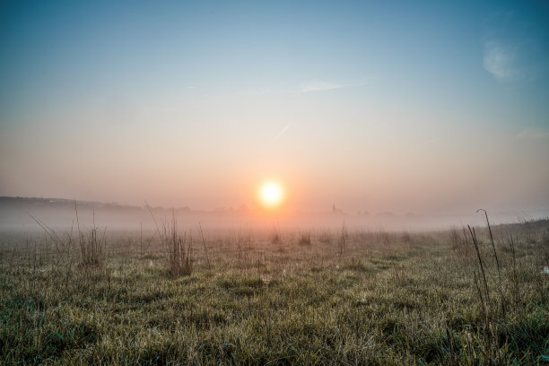 在一个有草和露水的田野里，一个有雾的早晨略带红色的日出图片下载